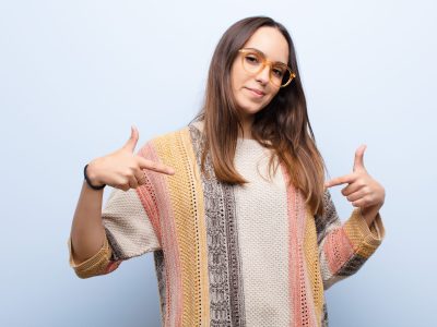 looking proud, arrogant, happy, surprised and satisfied, pointing to self, feeling like a winner young pretty woman looking proud, arrogant, happy, surprised and satisfied, pointing to self, feeling like a winner against blue wall