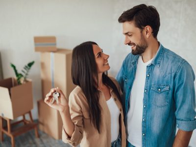 Young brunette lady looking at her male partner with love and affection while holding metal keys from a house